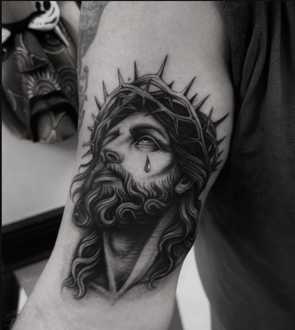 Black and gray Jesus portrait tattoo on upper arm by Danny Mac