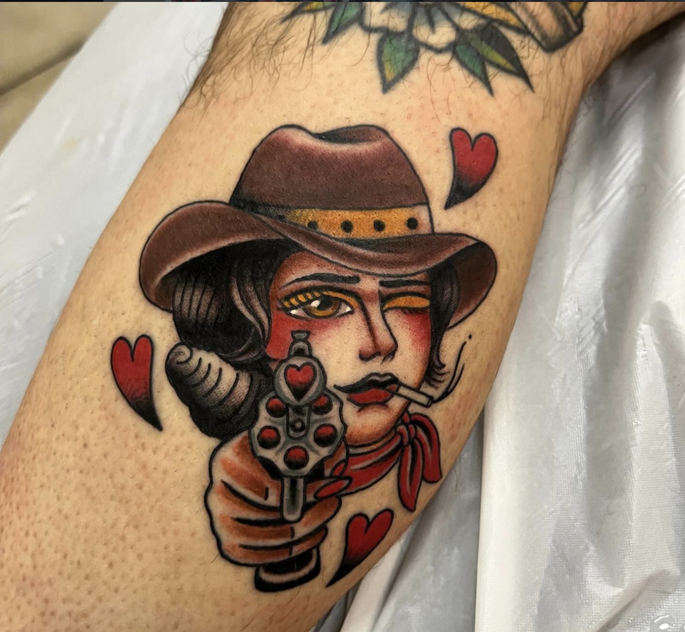 Traditional cowgirl with revolver and hearts calf tattoo by Danny Mac